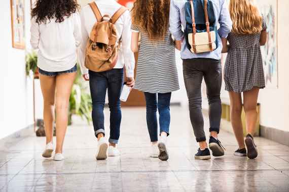 Group attractive teenage students in high school hall. Rear view.