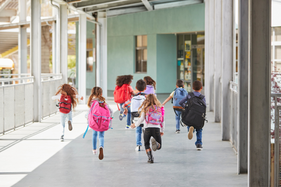 Volksschulkinder laufen mit Schultasche in die Schule