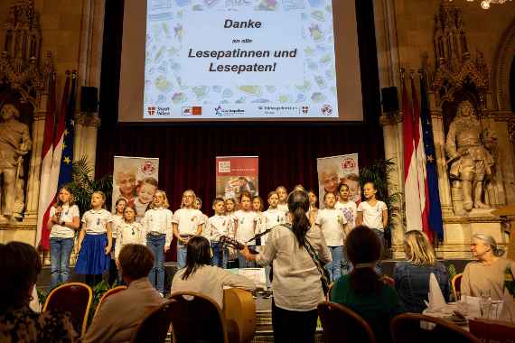 Ein Kinderchor - im Hintergrund liest man über eine Beamerprojektion "Danke-Fest für Wiener Lesepaten und Lesepatinnen"