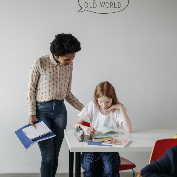 Eine Lehrerin steht hinter einer Schülerin und hat die Hand auf ihrem Rücken