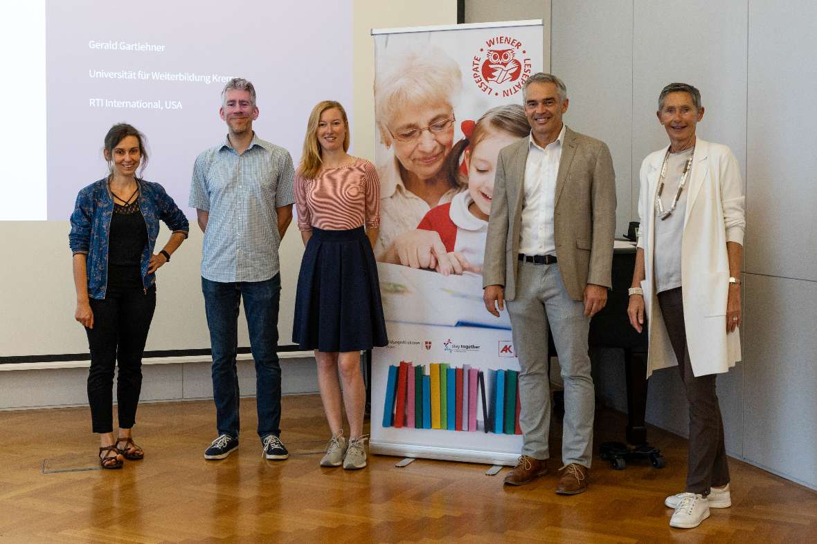 Die Vortragenden Iris Mair, BSc. MSc. BEd., MMag. Bernd Kerschner, Dr.med. Jana Meixner, MSc und Dr.med. Gerald Gartlehner, MPH sowie die Organisatorin Dr. Brigitte Scholz, stehen nebeneinander vor einem Aufsteller der Wiener Lesepat:innen.