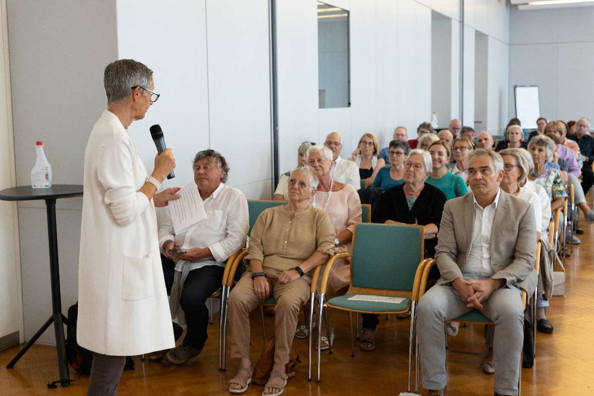 Die Organisatorin Dr. Brigitte Scholz steht vor dem Publikum und begrüßt die Gäste. 