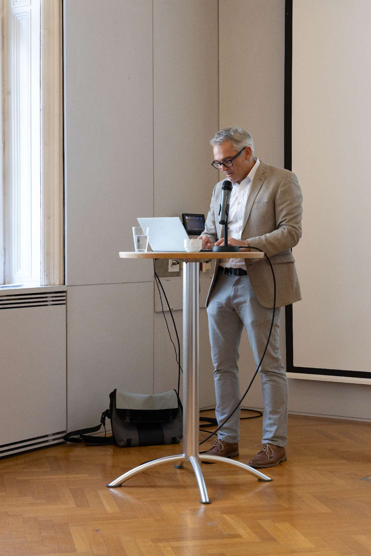 Dr.med. Gerald Gartlehner, MPH steht während seines Vortrages an einem Stehtisch mit einem Mikrofon und einem Laptop